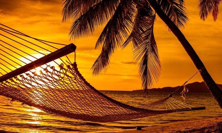 Hammock on the beach with palm trees at sunset