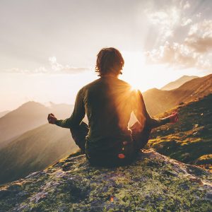 Man meditating in the mountains at sunset